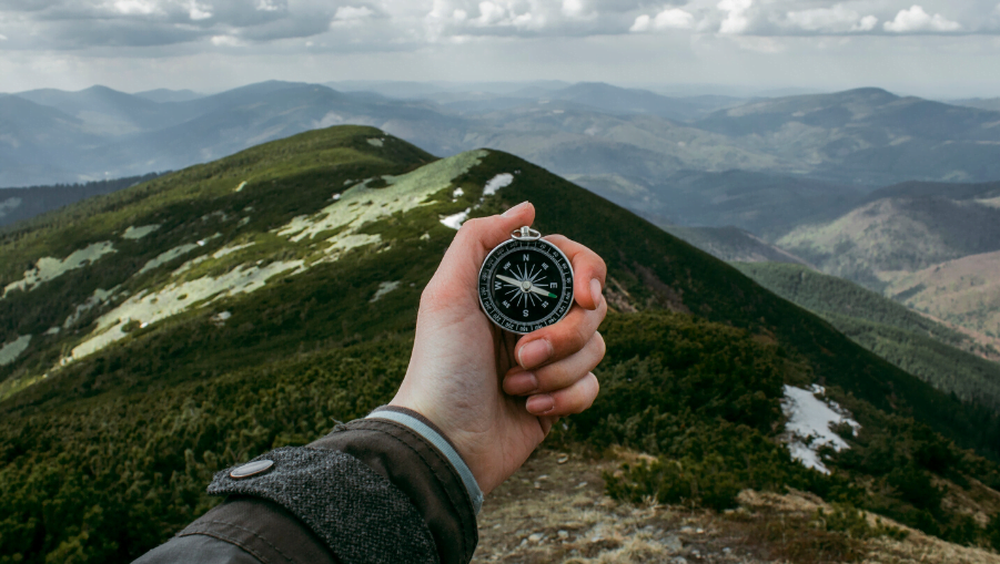 Image of a hand holding a compass on a mountain for the Modelling best & worst case scenarios to overcome inaccurate financial forecasts blog post by Brixx Software

