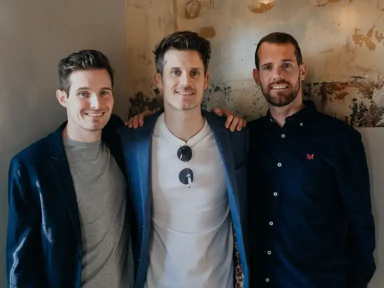 Group of three men smiling at a social gathering, casual attire, friendly atmosphere, urban backgrou.