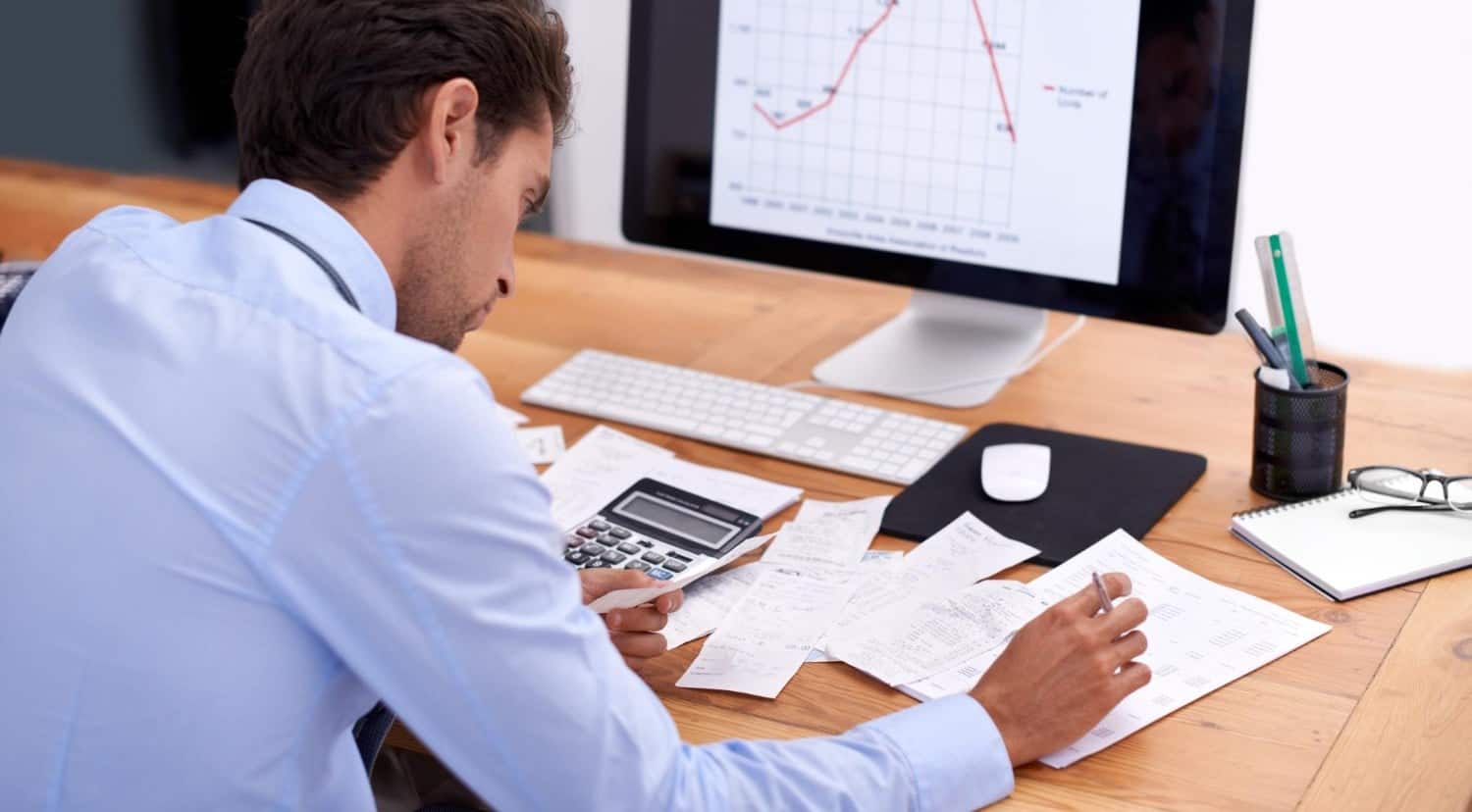 Business professional analysing financial data at desk with computer and documents.