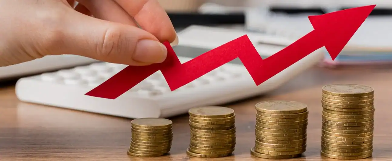 Business growth graph with rising red arrow and stacked coins on a desk.