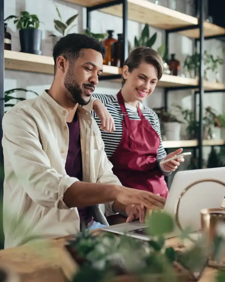 Friendly baristas preparing coffee in a modern café setting with plants and shelves.