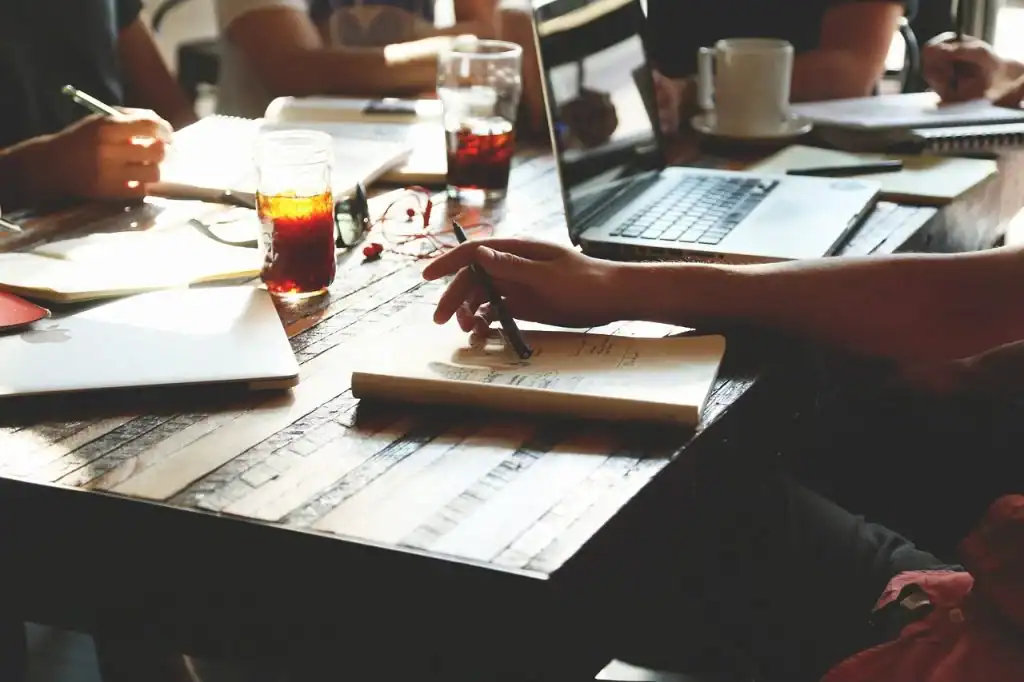 Collaborative business meeting with laptops, notebooks, and drinks at a modern workspace.