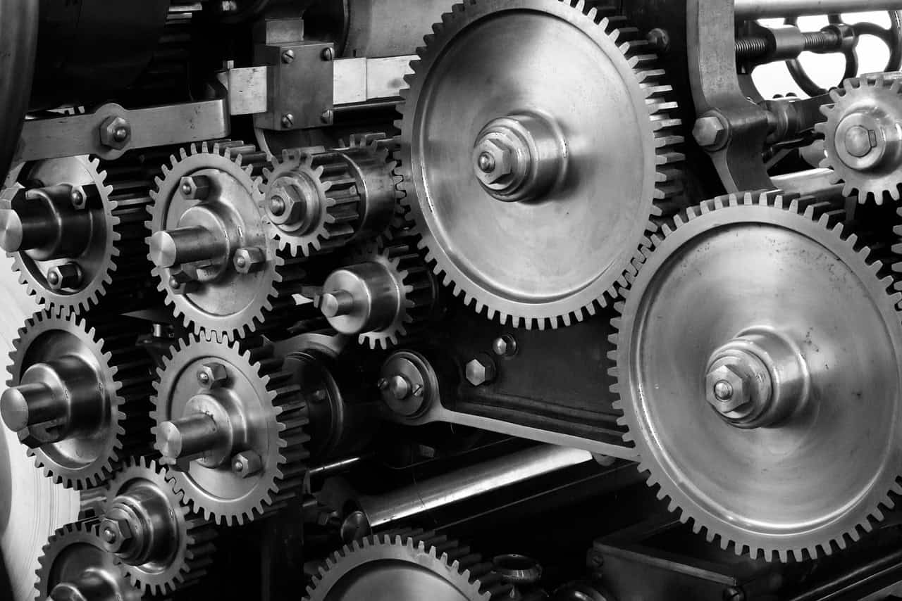 Complex gear system with interlocking cogs and wheels in black and white.