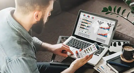 Business professional analysing data charts on laptop and smartphone for strategic planning.