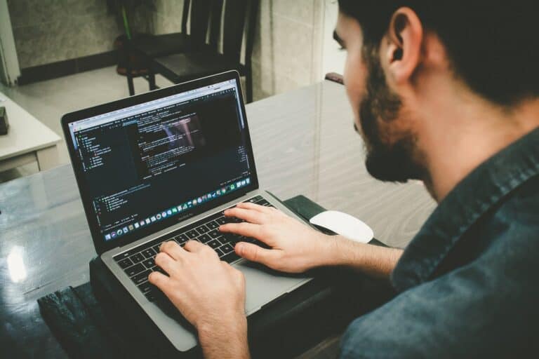 Developer coding on a laptop with programming code visible on screen.