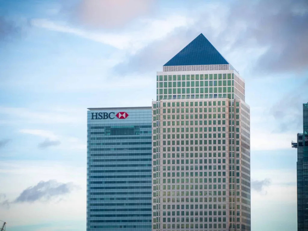 Modern office skyscraper with HSBC logo in a city skyline, featuring a pyramid-shaped top.
