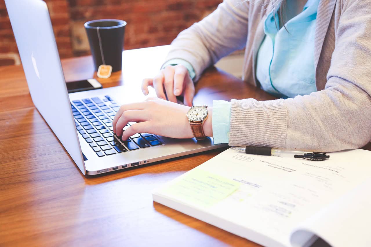 Person working on a laptop at a desk with documents and a coffee cup.