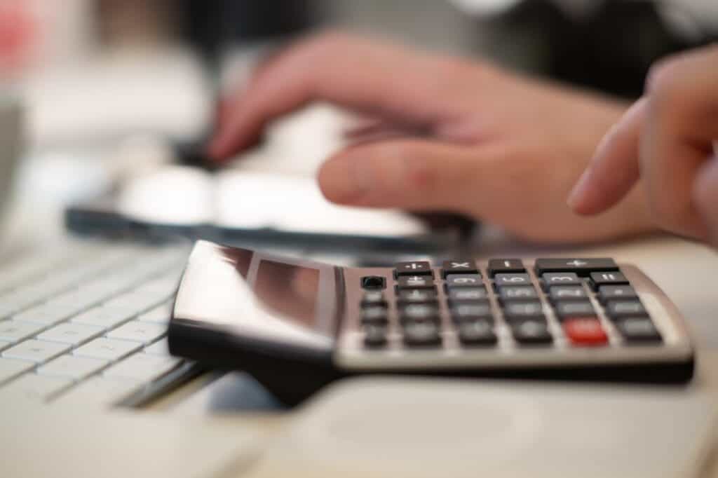 Person using calculator at desk with keyboard, focusing on financial calculations.